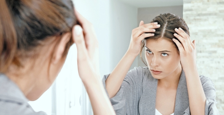 Женщина смотрит в зеркало на волосы