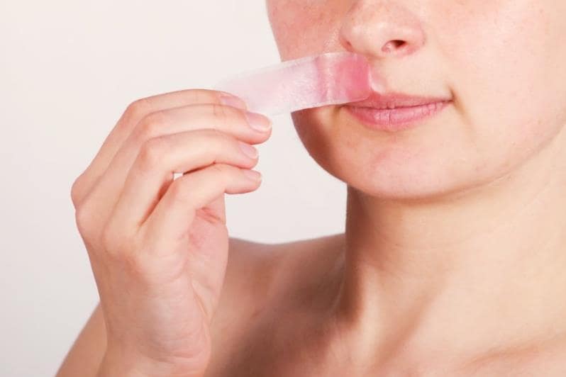 Девушка отдирает восковую полоску с лица