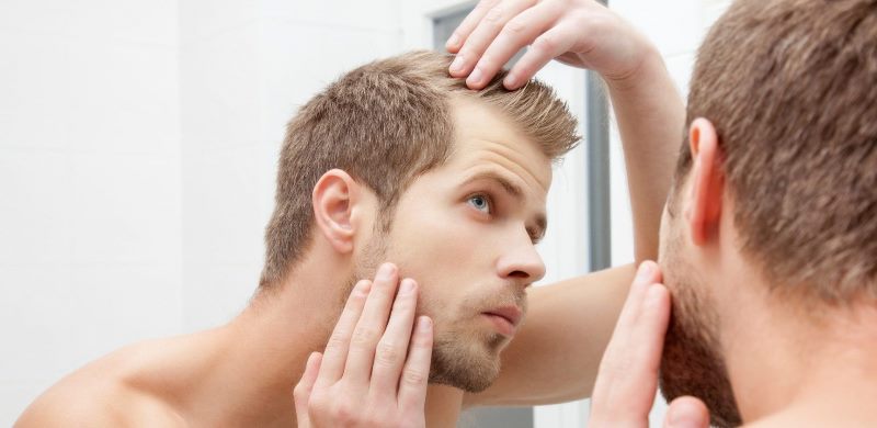 Мужчина смотрит в зеркало на волосы